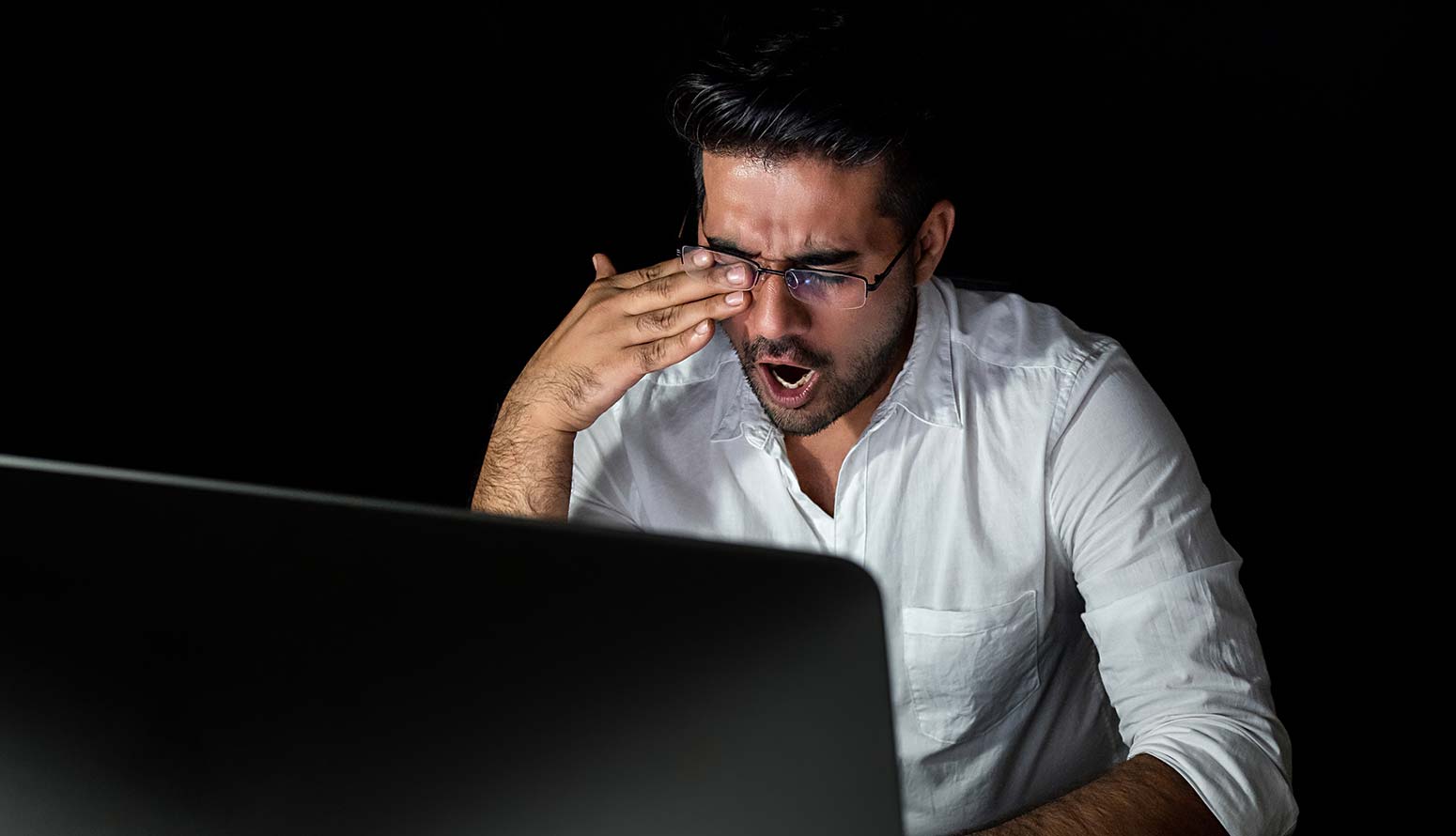 a man yawning while sitting in front of laptop